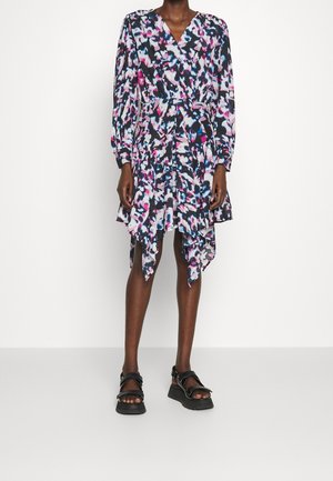 Mujer con un vestido de manga larga con estampado abstracto multicolor, con dobladillo asimétrico y sandalias negras con plataforma.
