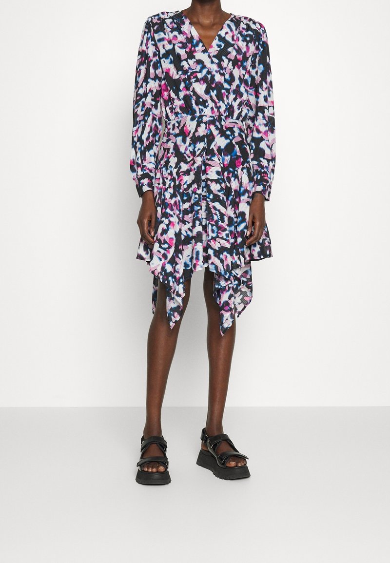 Femme portant une robe à manches longues à motif abstrait multicolore, avec un ourlet asymétrique et des sandales à plateforme noires.