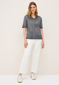 Haut gris à manches courtes et décolleté en V, présenté avec un jean large blanc et des baskets blanches. Texture douce, coutures minimales, coupe décontractée.