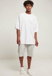 Hvid oversized t-shirt kombineret med grå shorts. Shortsene har sidelommer, og hvide sneakers fuldender looket. Enkel design og farver.