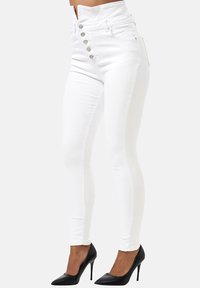 Jeans skinny blancos de tiro alto con una textura suave, cierre frontal de cinco botones y dos bolsillos. Combinados con zapatos de tacón negro de punta.