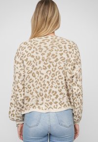 Donna con lunghi capelli biondi, che indossa un maglione a stampa leopardata beige e marrone e jeans azzurri chiari, vista di spalle.