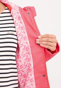 Rosa vattentät jacka med ett paisley-mönstrat foder. Har en dragkedja och tryckknappslås, med en svart och vit randig topp under.