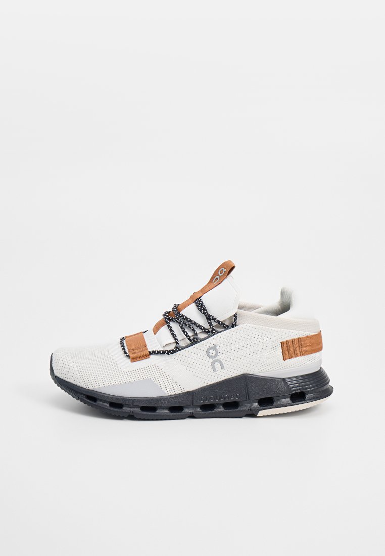 Weißes und braunes Sportschuh mit schwarzer segmentierter Sohle und gemusterten schwarzen Schnürsenkeln, seitlichem Logo und Netzoberfläche für Atmungsaktivität.