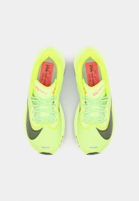 Neon yellow running shoes with mesh upper, black swoosh, and gray sole. Features flat laces and red branding on insoles.