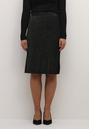 Jupe crayon noire en maille avec des paillettes métalliques, présentant une fente sur le côté, une longueur mi-mollet et une texture lisse. Portée avec des talons hauts noirs.