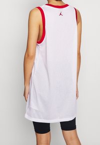 Vit nätvävd ärmlös tröja med röd kant, med rund urringning och sidoventiler, som visar en liten röd logotyp på baksidan.