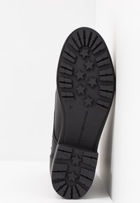 Botte en cuir noir avec une semelle en caoutchouc texturée présentant des motifs d'étoiles. La taille 37 est visible, ainsi que le logo Tommy Hilfiger.