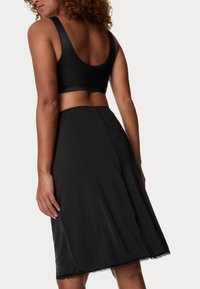 Černý bezramínkový crop top s kulatým zadním dílem, kombinovaný s černou sukní s krajkovým lemem a elastickým pasem.