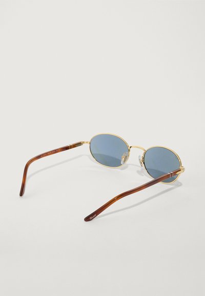 Ochelari de soare cu ramă aurie și lentile bleu, cu formă ovală și brațe din acetat maro cu un model subtil, oferind o estetică vintage.