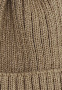 Berretto lavorato a maglia beige con texture a coste verticali e un bordo piegato. Realizzato in filato morbido, presenta un modello di maglia liscio e uniforme.