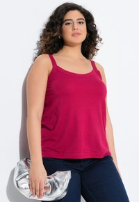 Ein magentafarbenes Tanktop mit breiten Trägern, einem runden Ausschnitt und einer lockeren Passform. Kombiniert mit dunkelblauen Jeans und einer metallischen silbernen Clutch.