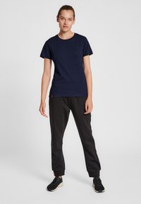 Mörkblå bomulls-T-shirt med korta ärmar, kombinerad med svarta joggingbyxor och svarta sportskor; modellen står i en neutral pose.