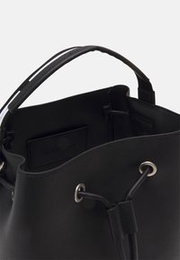 Černá kožená kabela ve tvaru kbelíku s utahovací šňůrkou, stříbrnými očky a hladkým povrchem. Interiér obsahuje malou kapsu.