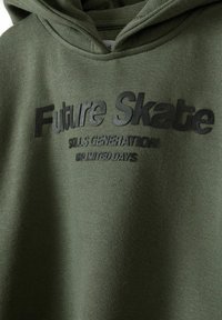 Sudadera color verde oliva con tejido texturizado. Presenta texto impreso "Generación Ilimitada de Habilidades de Skate Futuras" en negro. Capucha con cordones.