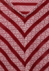 Tela de chevron en rojo y rosa con textura a cuadros; presenta bordes festoneados y pequeñas formas de diamante en blanco a lo largo.