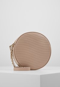 Runde beigefarbene Handtasche aus texturiertem Leder mit gewellten Linien, ausgestattet mit einem goldfarbenen Kettenhenkel und einem abnehmbaren Lederhandgelenktäschchen.