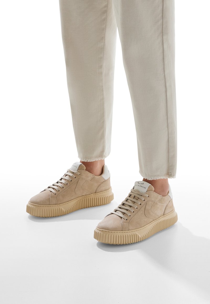 Sneaker in suede beige con dettagli testurizzati, punta rotonda e suola in gomma spessa. Lacci e un tab in contrasto sul tallone completano il design.