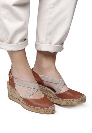 Brown leather wedge sandals with woven jute soles, featuring elastic cross-straps and a textured finish.