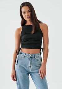 Musta röyhelö crop-top säädettävillä sivusiteillä, jossa on korkea kaulus. Yhdistetty vaaleansinisiin korkeavyötäröisiin suoriin farkkuihin.