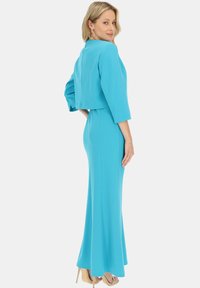 Dopasowana turkusowa sukienka z rozkloszowanym dołem, rękawami 3/4 oraz detalem krótkiej kurtki. Gładki, elegancki materiał w jednolitym kolorze.