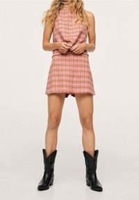 Abito scozzese rosa con design a crop top e gonna svasata. Indossato con stivali cowboy neri fino al ginocchio. Texture liscia, stile casual.