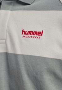 Tricou polo în dungi gri și alb cu logo roșu "hummel SPORTSWEAR" pe piept.