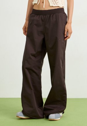 Lockere schwarze Nike-Trainingshose mit elastischem Bund, getragen mit weißen Sneakers und einem kurzen Strick-Top.