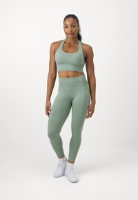 Tenue de sport vert clair composée d'un crop top et de leggings taille haute. Le tissu semble lisse avec un design sans couture.