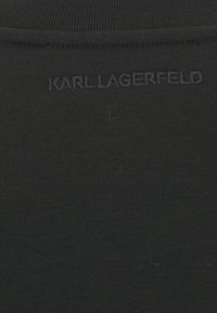 Tessuto nero con una superficie liscia caratterizzato dal testo ricamato "KARL LAGERFELD" in un filo scuro abbinato sul retro.