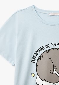 Camiseta de manga corta de color azul claro, hecha de un material suave, con un diseño de cartoon impreso de un animal durmiendo y el texto "SOÑANDO CONTIGO".