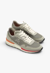 Graue Sneaker aus Stoff und Wildleder. Sie verfügen über ein Skull-Logo, cremeweiße Schnürsenkel, orangefarbene und rote Akzente an der Sohle sowie ein strukturiertes Design.