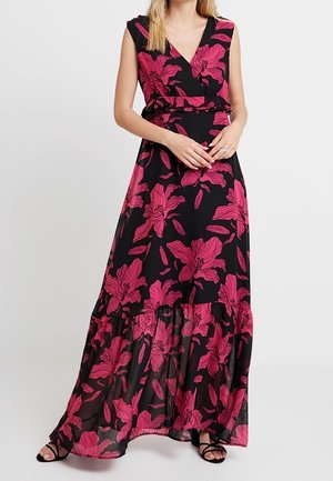 Robe maxi noire sans manches avec un grand imprimé floral rose vif, col en V, taille cintrée et ourlet transparent à volants, portée avec des sandales noires à fines lanières.