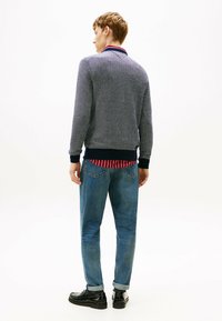 Maglione da uomo in maglia blu navy testurizzata con colletto a righe rosse e bianche; abbinato a jeans azzurri chiari e scarpe nere. Design semplice e casual.