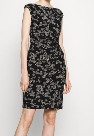 Zwart mouwloos jurkje tot op de knieën met een getailleerde taille en een zilverkleurig bloemmotief, gedragen door een staande persoon tegen een effen achtergrond.