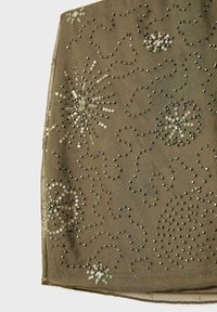 Zeleni materijal s spiralnim i cvjetnim uzorcima od metalnih perlica i špirala, sa glatkom teksturom i delikatnim detaljima šivanja.