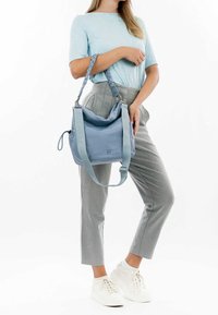 Sac à épaule bleu clair en tissu doux, avec un design décontracté, une bandoulière réglable et un logo embossé sur le côté.