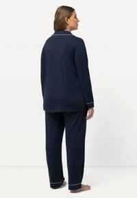 Completo pigiama blu navy realizzato in tessuto morbido; presenta maniche lunghe, piping bianco su polsini e colletto, e pantaloni svasati.