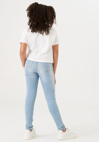 Weißes, gekürztes T-Shirt und hellblaue Skinny-Jeans. Weicher Stoff, taillierte Passform, minimale Abnutzung und Gesäßtaschen. Weiße Sneaker.