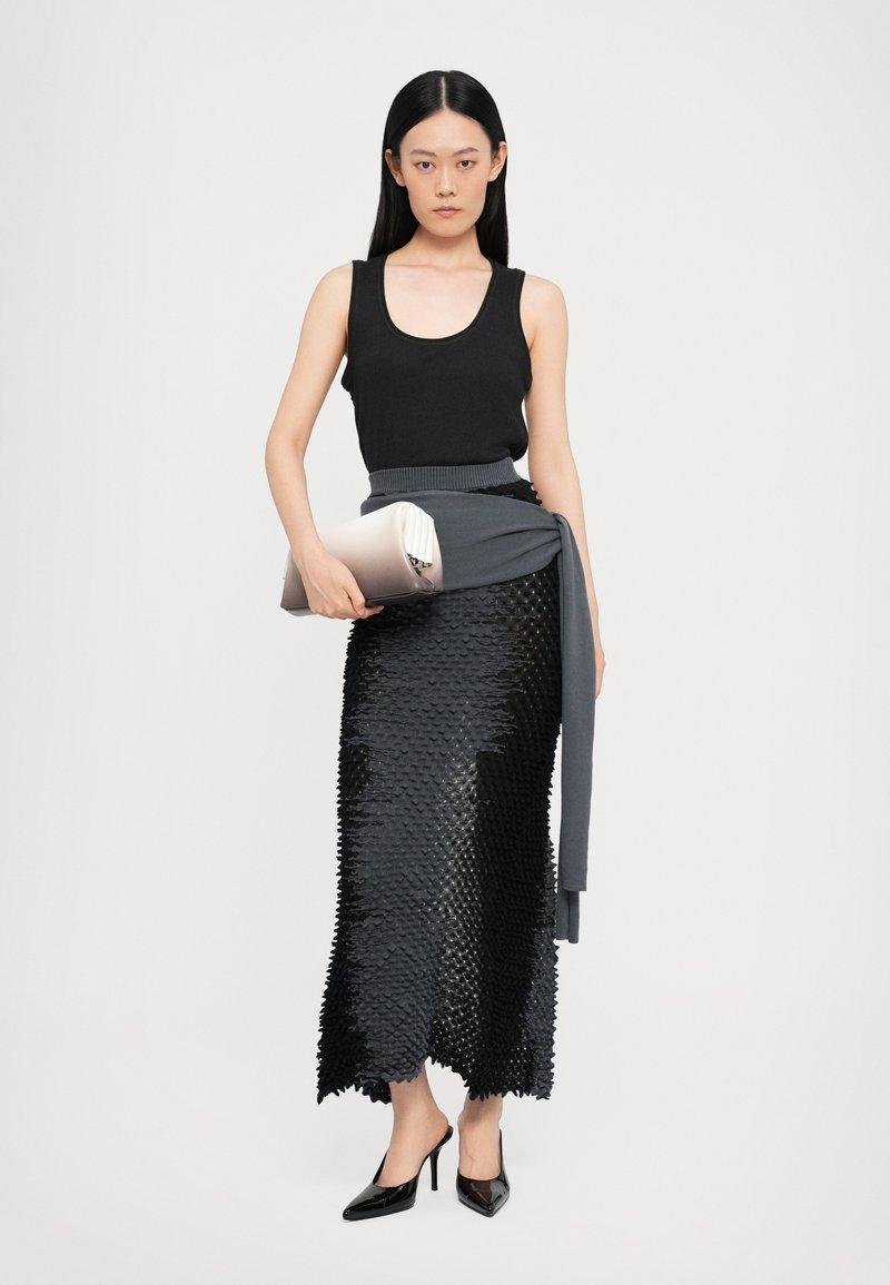 Top nero a canotta abbinato a una gonna nera tessurizzata con orlo a scallop. Gli accessori comprendono un'cappotto grigio e una pochette metallica. Scarpe con tacco alto.
