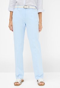 Lichtblauwe, op maat gemaakte broek met een gladde textuur, voorzien van zijzakken en een witte riem. Gecombineerd met witte sandalen met banden.
