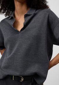 Polo shirt grigio scuro in maglia con colletto, maniche corte e un parziale bottonatura. La texture sembra morbida e ha una vestibilità rilassata.