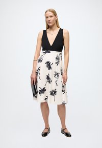 Juodos ir baltos spalvų gėlių raštų suknelė su gilia V formos iškirpte, aptemu liemeniu ir lengvai krentančia suknele. Derinama su juoda delninuke ir blizgiais juodais batais.