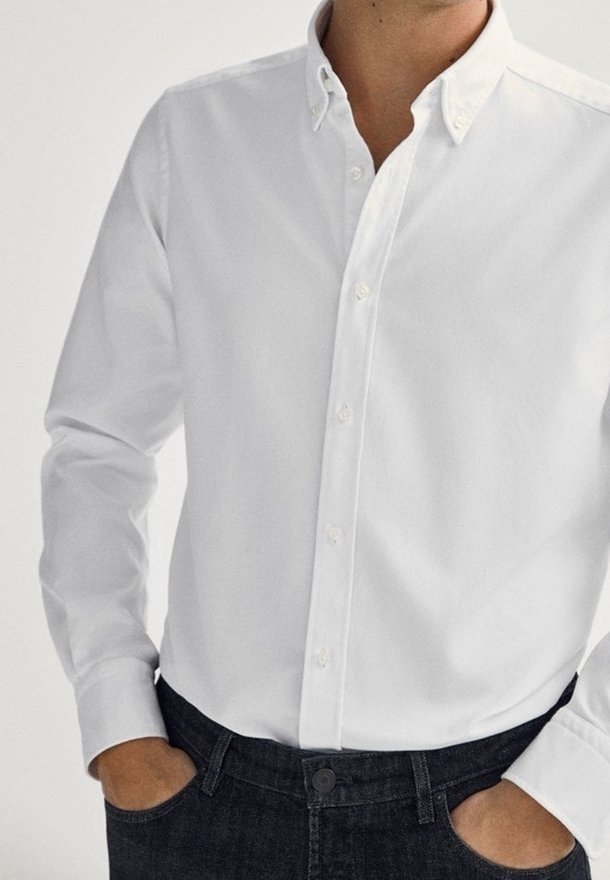 Camicia bianca a maniche lunghe con colletto, dal tessuto liscio, abbinata a jeans in denim scuri.