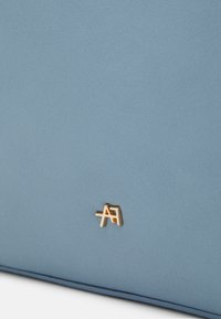 Modrá kožená taška s texturou, na přední straně s malým zlatým logem, čisté linie a hladký povrch.