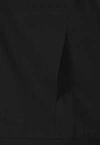 Gros plan sur un tissu noir texturé avec des coutures visibles et un détail de pli.