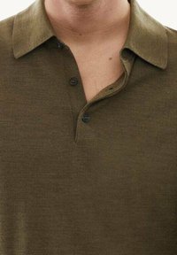 Olive green polo shirt crafted from a soft fabric, featuring a classic collar, three black buttons, and a textured knit design.