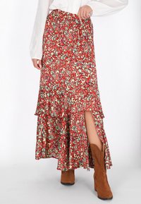 Fustă maxi cu un model roșu și verde, cu un design stratificat, talie elastica și decupaj lateral, asortată cu cizme scurte din ante maro.