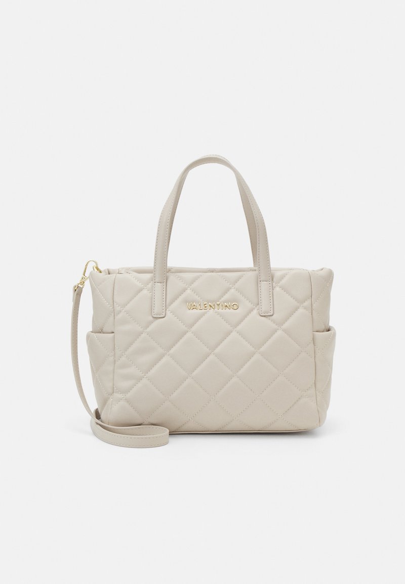 Quilted beige handbag with dual handles and a removable shoulder strap. Features gold logo on front and external side pockets.