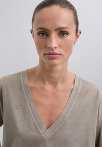 Camiseta de algodón en color topo, con cuello en V y mangas cortas, textura suave y costuras visibles a lo largo del escote y las mangas.